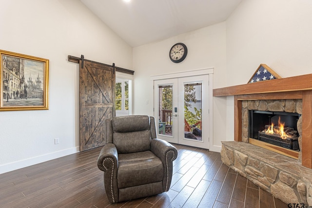 living area featuring a stone fireplace, french doors, a barn door, high vaulted ceiling, and dark hardwood / wood-style floors