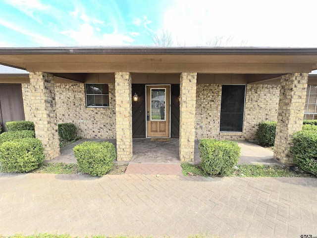 entrance to property featuring brick siding and covered porch