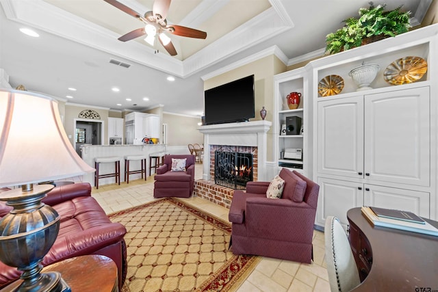 tiled living room featuring a brick fireplace, ceiling fan, built in features, and ornamental molding