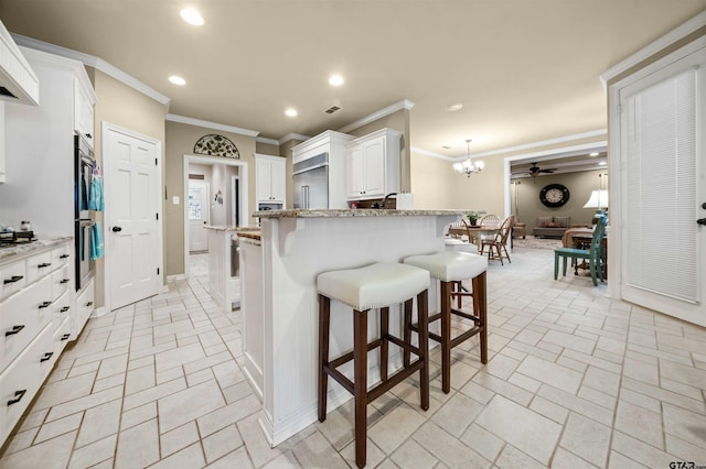 kitchen featuring a kitchen breakfast bar, light stone countertops, white cabinetry, and crown molding