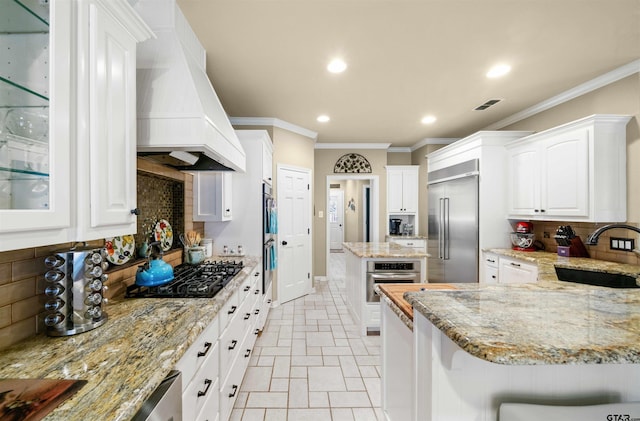 kitchen featuring built in refrigerator, sink, white cabinetry, black gas cooktop, and premium range hood