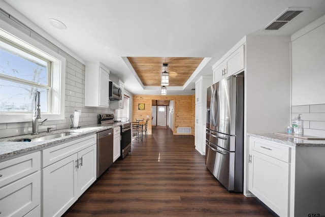 kitchen featuring appliances with stainless steel finishes, sink, white cabinets, backsplash, and light stone countertops