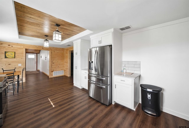 kitchen with white cabinets, a raised ceiling, stainless steel fridge, and wooden walls