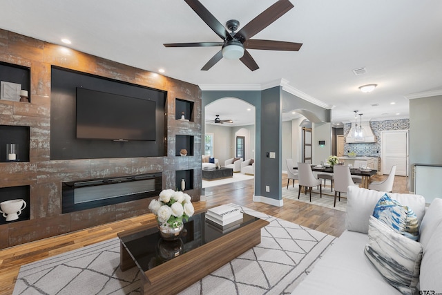 living area featuring ornamental molding, ceiling fan, wood finished floors, arched walkways, and a large fireplace