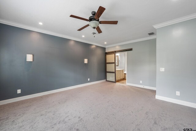 unfurnished room with ornamental molding, a barn door, visible vents, a ceiling fan, and baseboards