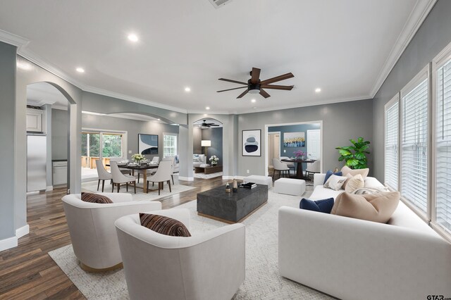living area with wood finished floors, a ceiling fan, arched walkways, ornamental molding, and recessed lighting