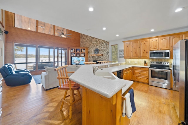 kitchen featuring sink, light hardwood / wood-style flooring, kitchen peninsula, a breakfast bar, and appliances with stainless steel finishes