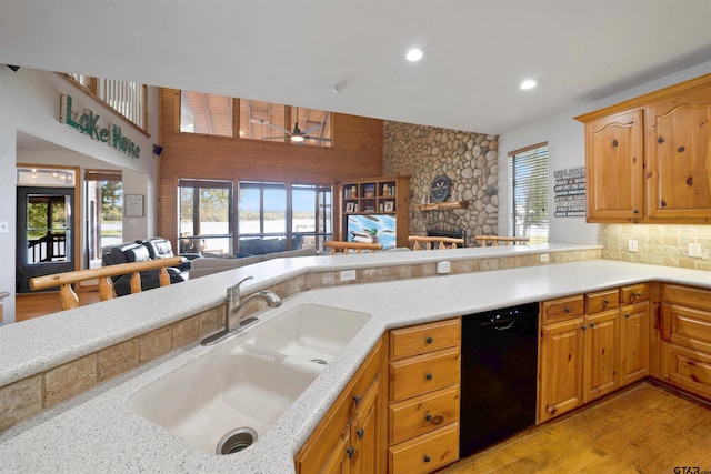 kitchen featuring kitchen peninsula, light wood-type flooring, sink, black dishwasher, and a stone fireplace