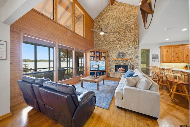 living room with ceiling fan, light wood-type flooring, a fireplace, and high vaulted ceiling