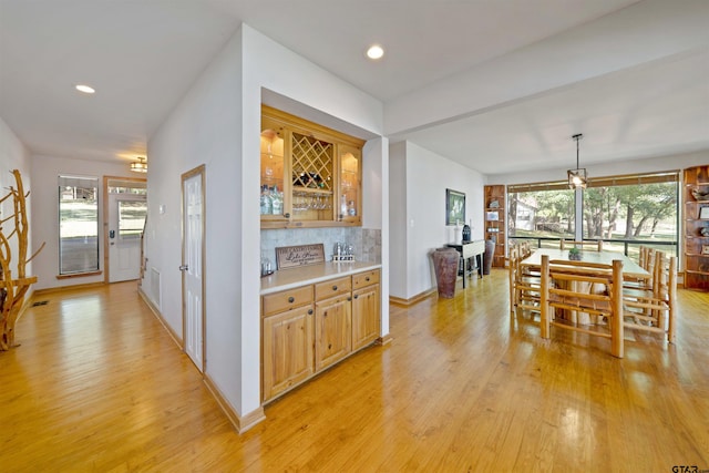 kitchen with light wood-type flooring, decorative light fixtures, plenty of natural light, and backsplash