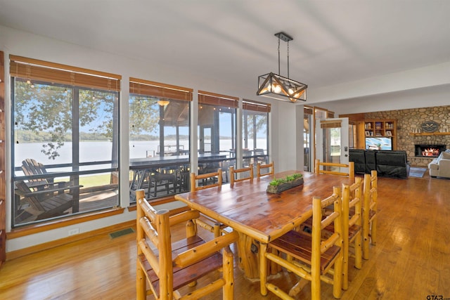 dining room with a stone fireplace, plenty of natural light, a water view, and light hardwood / wood-style floors