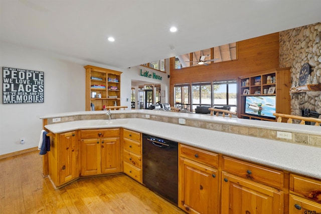 kitchen with light wood-type flooring, ceiling fan, sink, black dishwasher, and a stone fireplace