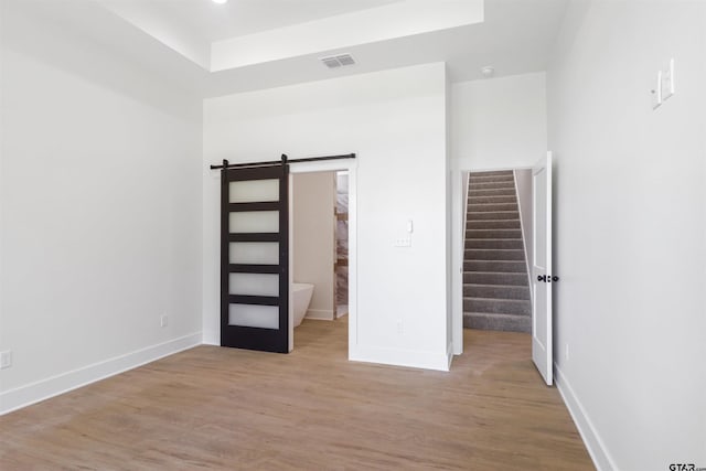 unfurnished bedroom featuring a barn door, light hardwood / wood-style floors, and connected bathroom