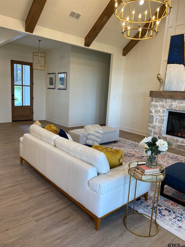 living room featuring beamed ceiling, wood-type flooring, a stone fireplace, and a notable chandelier