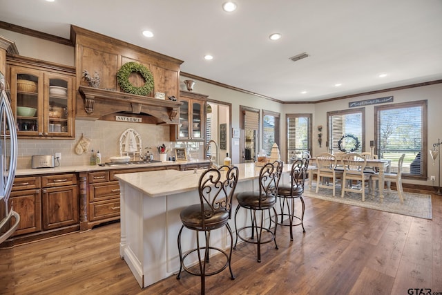 kitchen with stainless steel appliances, backsplash, wood-type flooring, a kitchen island with sink, and a breakfast bar