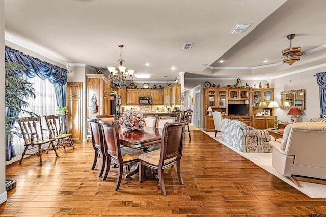 dining area featuring ceiling fan with notable chandelier, light hardwood / wood-style floors, a raised ceiling, and crown molding