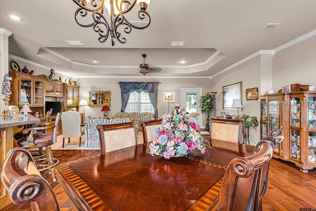 dining space with a tray ceiling, hardwood / wood-style floors, ceiling fan with notable chandelier, and crown molding