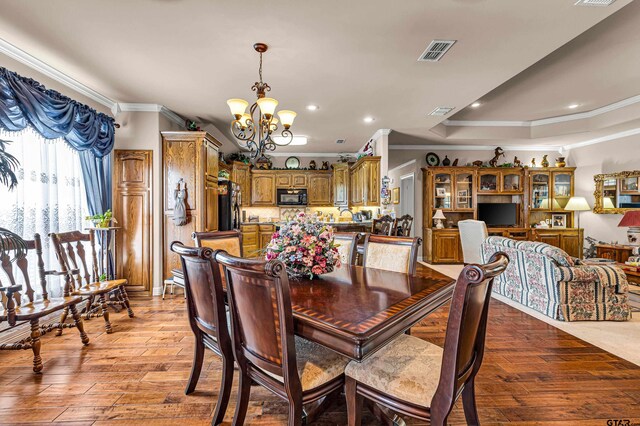 dining space featuring a tray ceiling, light wood-type flooring, a chandelier, and crown molding