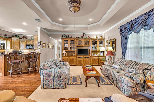 living room with ceiling fan, a tray ceiling, crown molding, and light hardwood / wood-style flooring