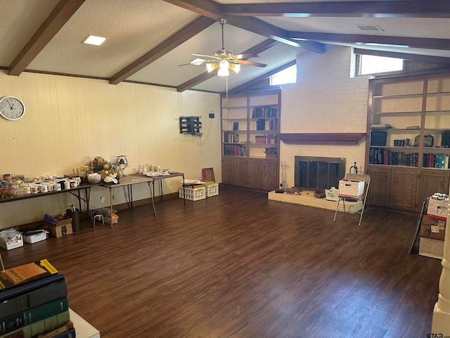 interior space with ceiling fan, a textured ceiling, a fireplace, vaulted ceiling with beams, and dark wood-type flooring