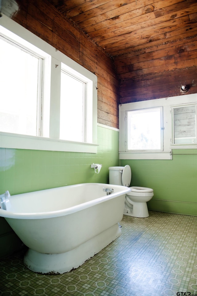 bathroom with toilet, vaulted ceiling, wood ceiling, wood walls, and a tub to relax in