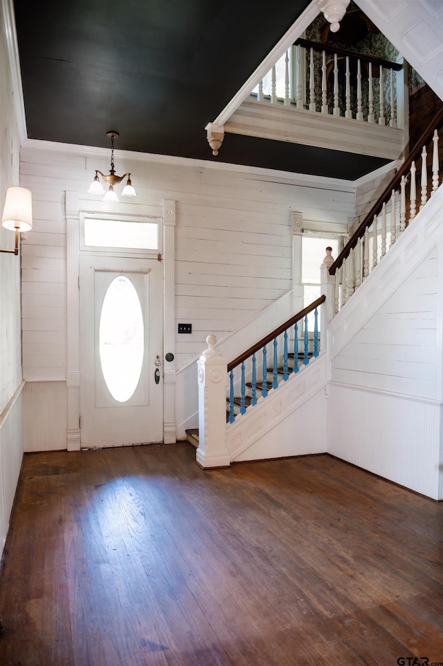 entryway featuring a wealth of natural light, dark wood-type flooring, wooden walls, and an inviting chandelier