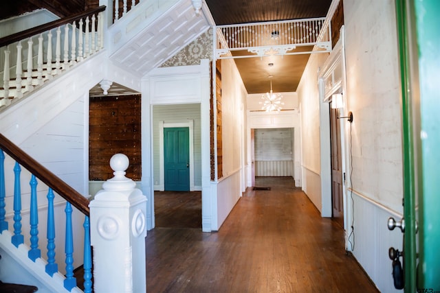 hallway featuring dark hardwood / wood-style flooring, wood walls, high vaulted ceiling, and a chandelier