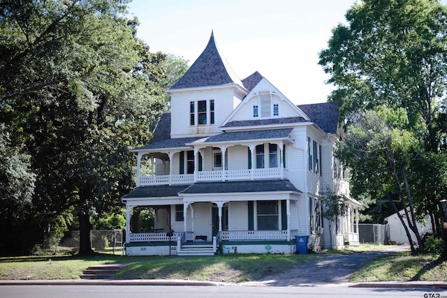 victorian house with covered porch, a front yard, and a balcony