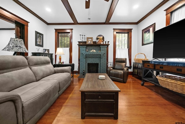 living room featuring light wood-type flooring, ceiling fan, beamed ceiling, and a brick fireplace