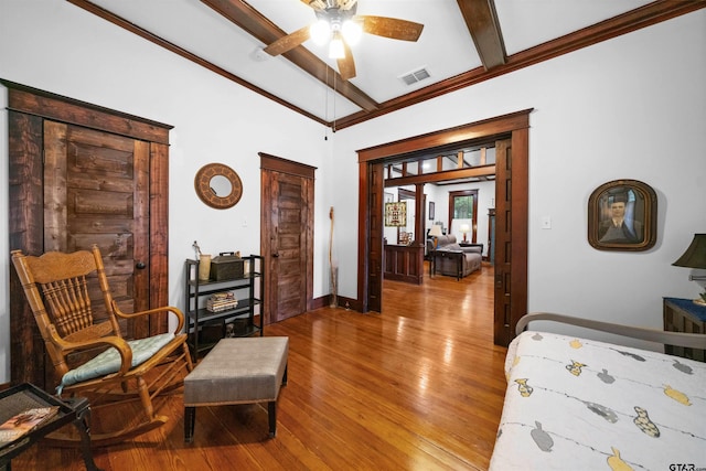 bedroom featuring ceiling fan, beamed ceiling, ornamental molding, and wood-type flooring