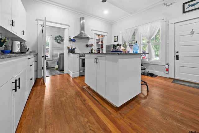 kitchen featuring white cabinets, a kitchen island, wall chimney range hood, tasteful backsplash, and a breakfast bar