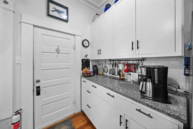 kitchen featuring white cabinetry, decorative backsplash, ornamental molding, dark wood-type flooring, and dark stone counters