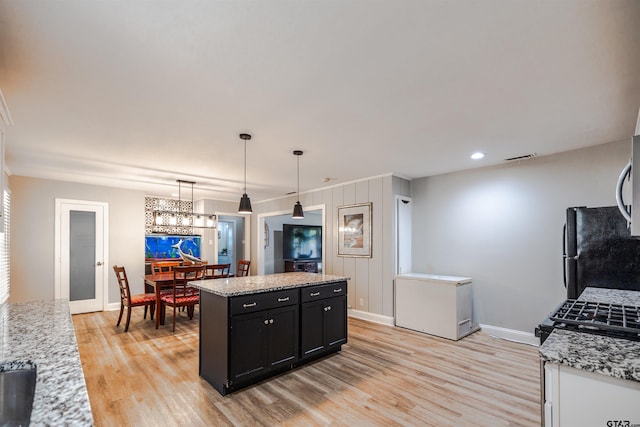 kitchen with black fridge, light stone counters, a kitchen island, light wood-type flooring, and pendant lighting