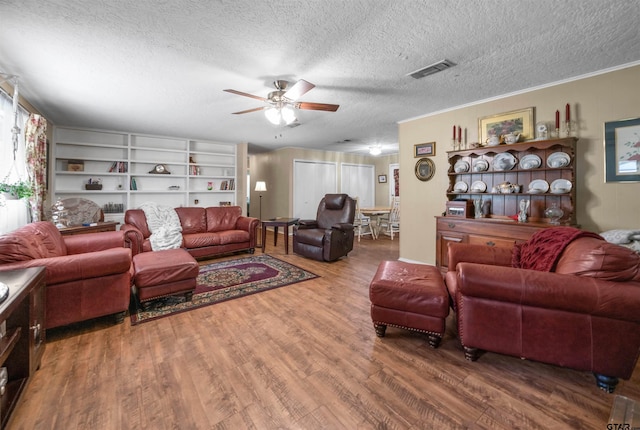 living room featuring ceiling fan, built in features, wood-type flooring, a textured ceiling, and ornamental molding