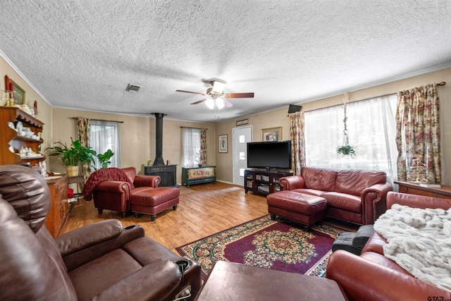 living room with a wood stove, ceiling fan, crown molding, and hardwood / wood-style flooring