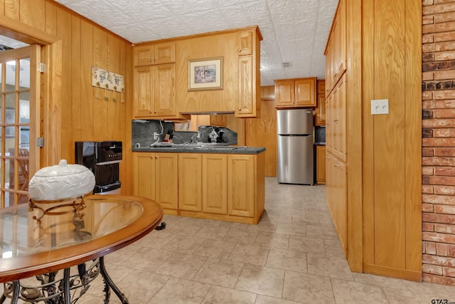 kitchen with wood walls, light brown cabinetry, stainless steel refrigerator, and a textured ceiling