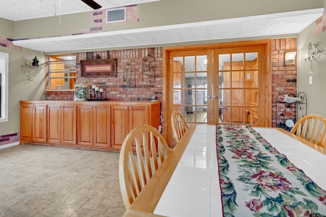 dining area featuring french doors, brick wall, ceiling fan, and light tile patterned floors