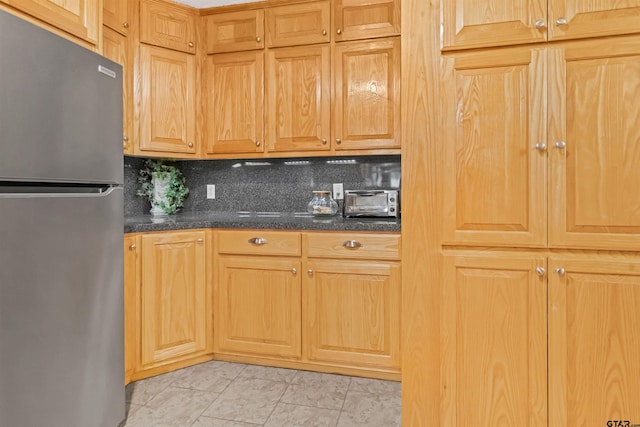 kitchen with dark stone countertops, decorative backsplash, and stainless steel refrigerator