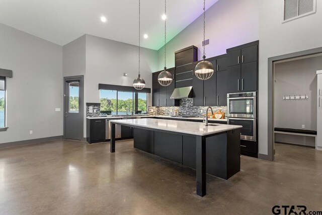 kitchen featuring visible vents, finished concrete flooring, a high ceiling, wall chimney range hood, and appliances with stainless steel finishes