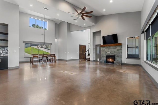 living room featuring concrete floors, a high ceiling, a ceiling fan, and a stone fireplace