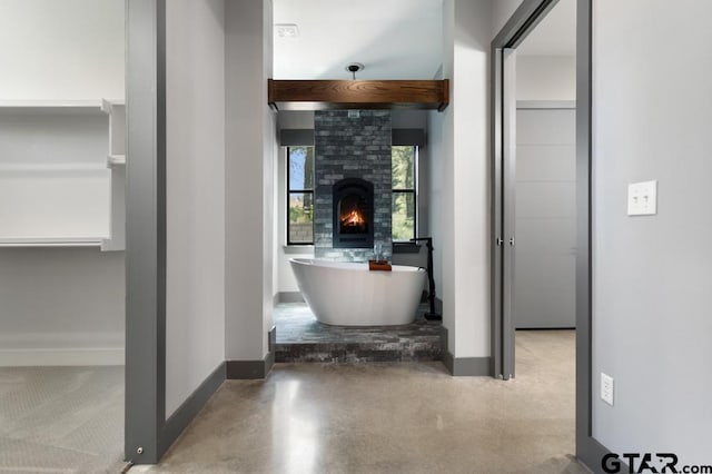 interior space featuring a warm lit fireplace, a freestanding tub, finished concrete flooring, and baseboards
