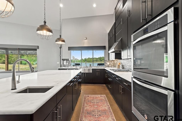 kitchen with stainless steel appliances, a sink, wall chimney exhaust hood, tasteful backsplash, and hanging light fixtures