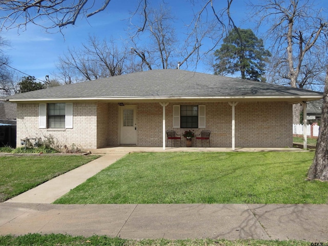 ranch-style home with a front yard, covered porch, brick siding, and roof with shingles