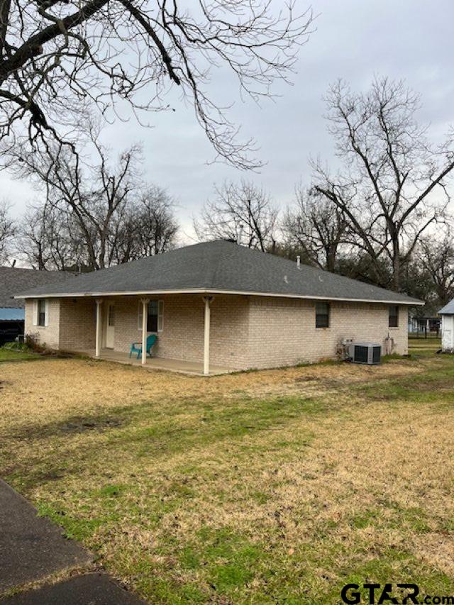 rear view of property featuring brick siding, central air condition unit, and a lawn