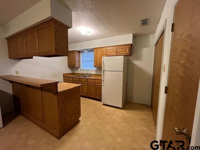 kitchen with visible vents, a sink, a textured ceiling, freestanding refrigerator, and a peninsula