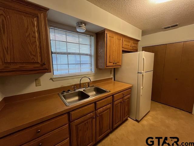 kitchen featuring visible vents, light floors, freestanding refrigerator, a textured ceiling, and a sink