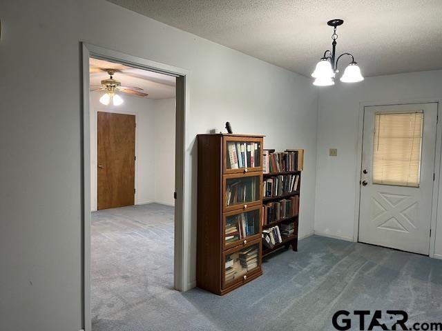 foyer entrance featuring a notable chandelier, carpet flooring, and a textured ceiling