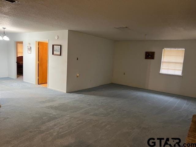 empty room with a notable chandelier, light colored carpet, and a textured ceiling