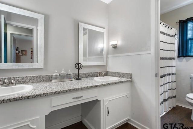 bathroom featuring toilet, double vanity, a sink, and wood finished floors