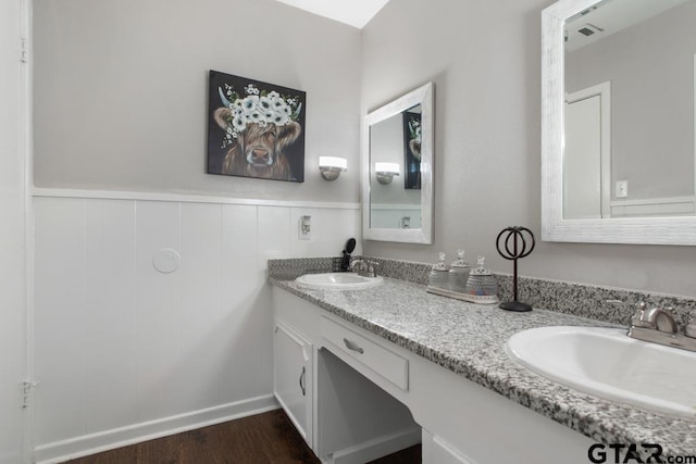 bathroom with double vanity, wood finished floors, a sink, and wainscoting